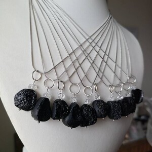 May include: A set of ten necklaces with black lava rock pendants and clear crystal accents. Each necklace features a silver chain.