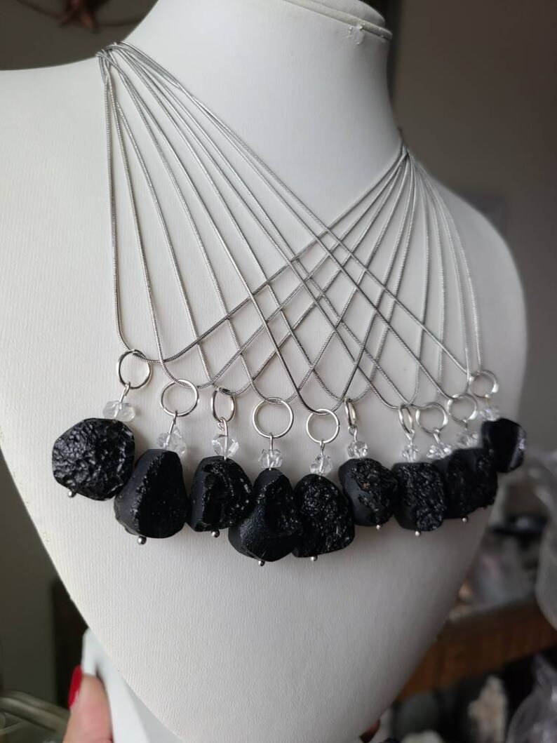 May include: A set of ten necklaces with black lava rock pendants and clear crystal accents. Each necklace features a silver chain.