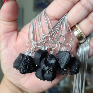 May include: A group of black obsidian pendants on silver chains. Each pendant has a clear crystal charm attached.