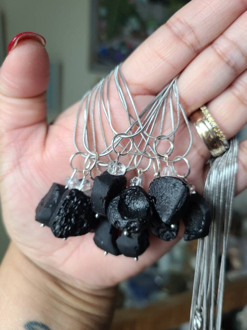 May include: A group of black obsidian pendants on silver chains. Each pendant has a clear crystal charm attached.