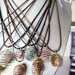 May include: A set of six necklaces with gold wire cages containing various colored stones. The necklaces are made with brown and black cords.