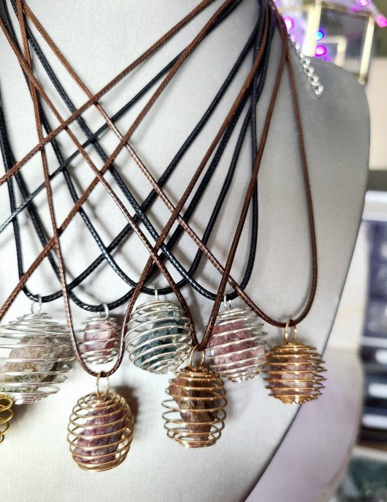 May include: A set of six necklaces with gold wire cages containing various colored stones. The necklaces are made with brown and black cords.
