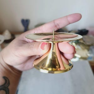 Pu&ograve; includere: Un piccolo portacandele dorato con base rotonda e stelo svasato e conico. La parte superiore presenta una superficie circolare piatta con una punta centrale per tenere una candela. Il portacandele &egrave; in metallo lucido.