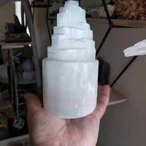 Op de afbeelding: Een witte selenietkristaltoren met een gelaagd, gestapelde ontwerp. De kristal is glad en gepolijst, met een doorschijnende uitstraling.