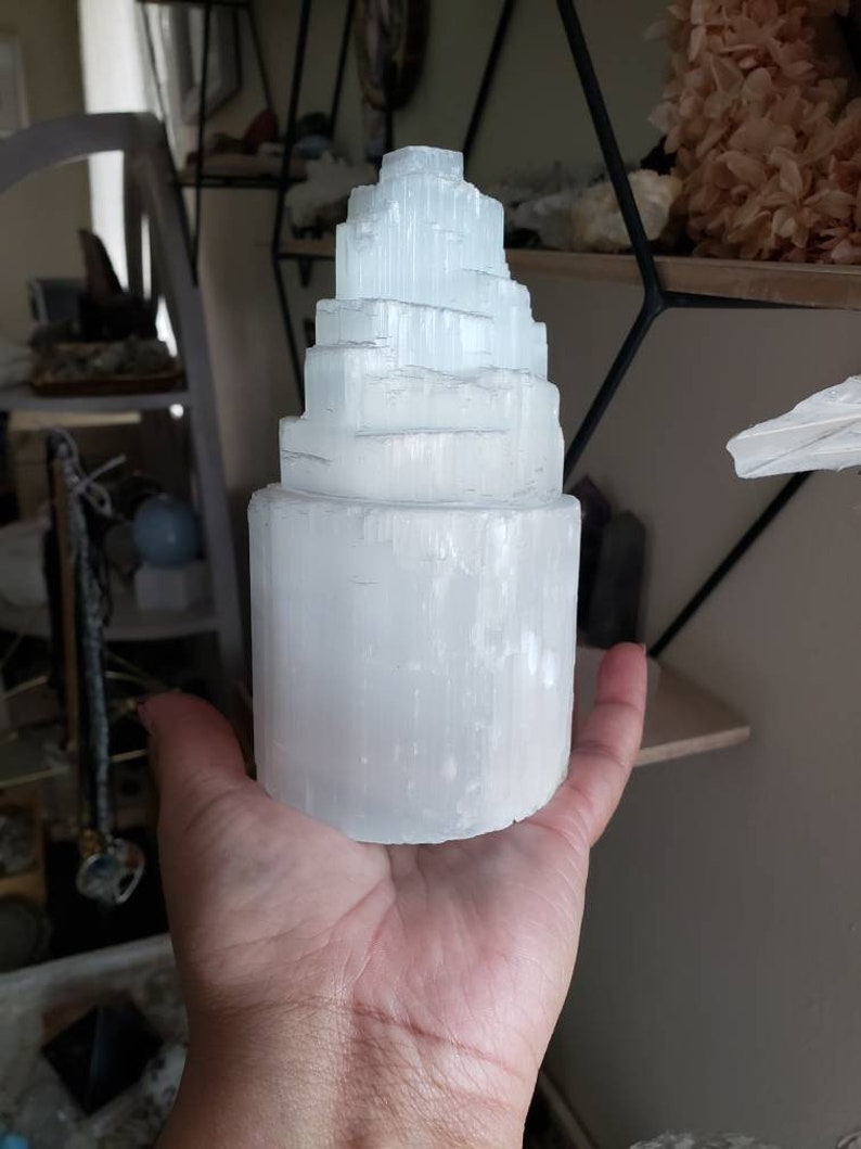 Op de afbeelding: Een witte selenietkristaltoren met een gelaagd, gestapelde ontwerp. De kristal is glad en gepolijst, met een doorschijnende uitstraling.