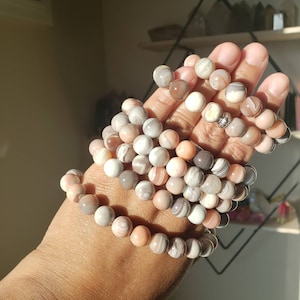 Op de afbeelding: Een stapel armbanden gemaakt van agaat kralen in tinten roze, wit en grijs. De kralen hebben een natuurlijk, gemarmerd patroon.