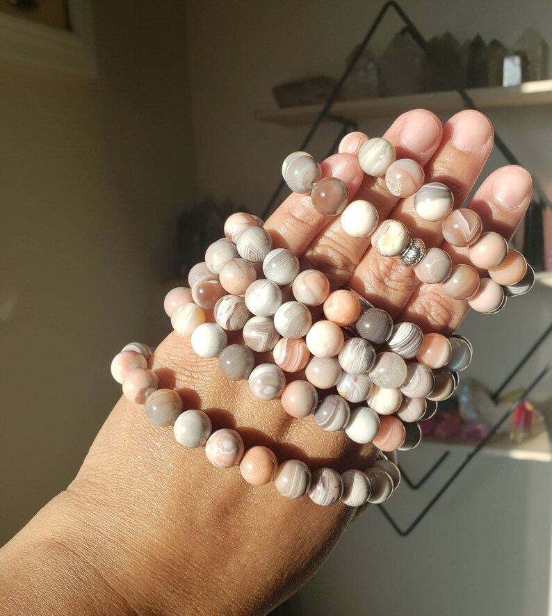 Op de afbeelding: Een stapel armbanden gemaakt van agaat kralen in tinten roze, wit en grijs. De kralen hebben een natuurlijk, gemarmerd patroon.