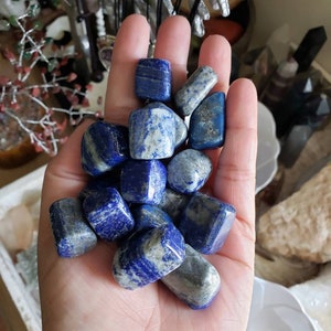 May include: A collection of tumbled lapis lazuli stones in various shades of blue and white. The stones are smooth and polished, with a natural, irregular shape.
