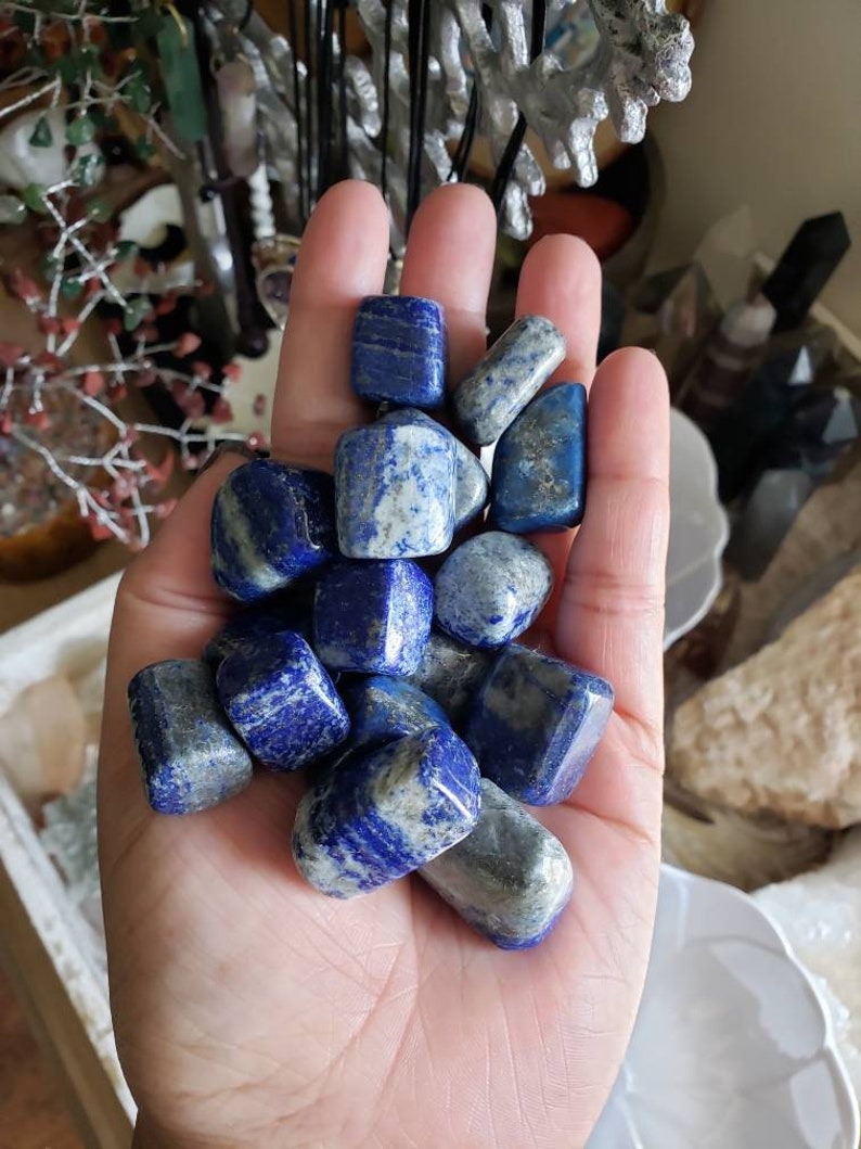 May include: A collection of tumbled lapis lazuli stones in various shades of blue and white. The stones are smooth and polished, with a natural, irregular shape.