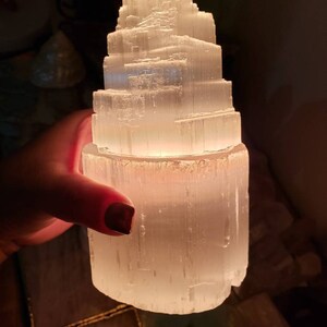 Op de afbeelding: Een witte selenietkristal lamp in de vorm van een piramide met een warme gloed die uit de basis komt.