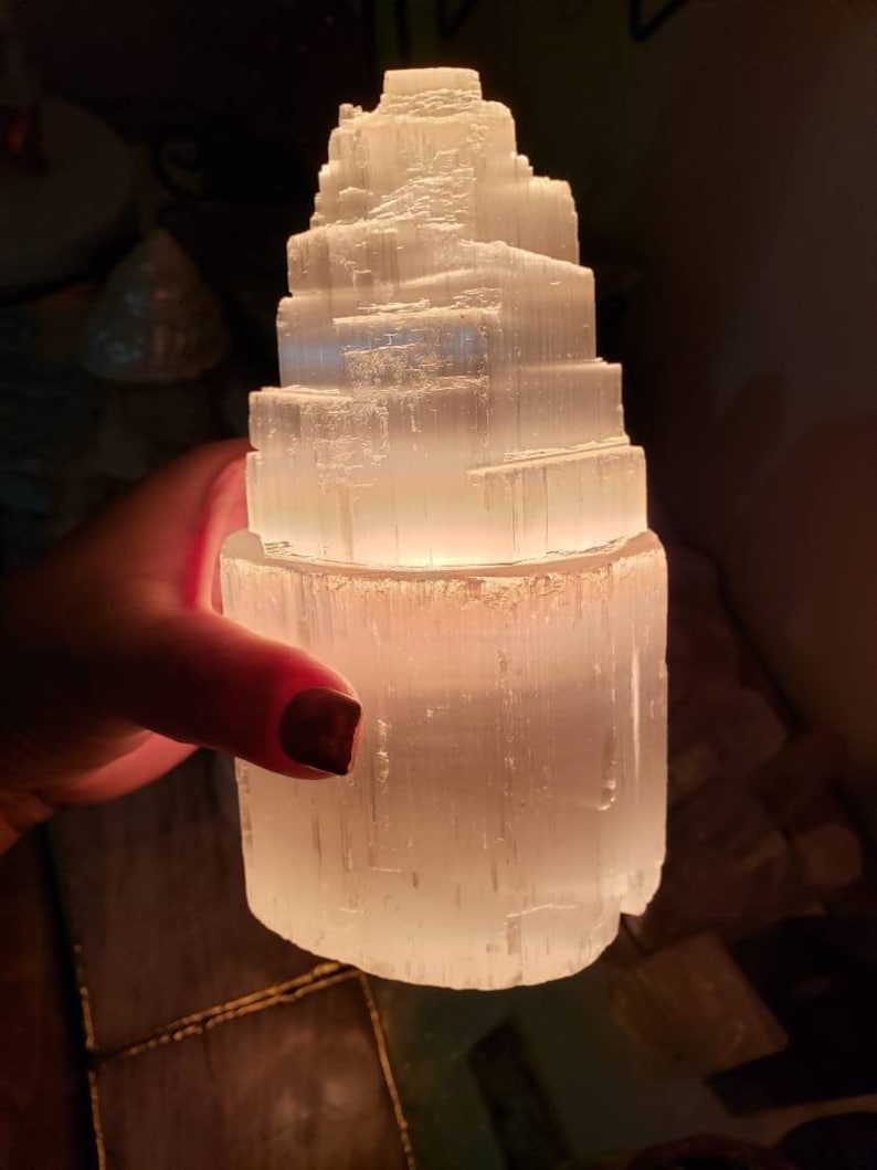 Op de afbeelding: Een witte selenietkristal lamp in de vorm van een piramide met een warme gloed die uit de basis komt.