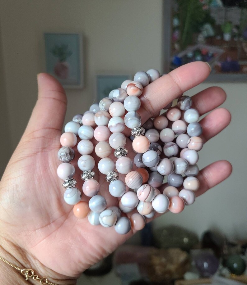 Op de afbeelding: Een stapel armbanden gemaakt van roze en grijze agaat kralen met zilveren accenten.