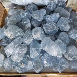 Peut inclure: Une collection de pierres de calcite bleue brutes et polies avec un aspect cristallin translucide. Les pierres varient en taille et en forme, pr&eacute;sentant des nuances de bleu p&acirc;le &agrave; moyen avec des fractures internes naturelles et des surfaces lisses.