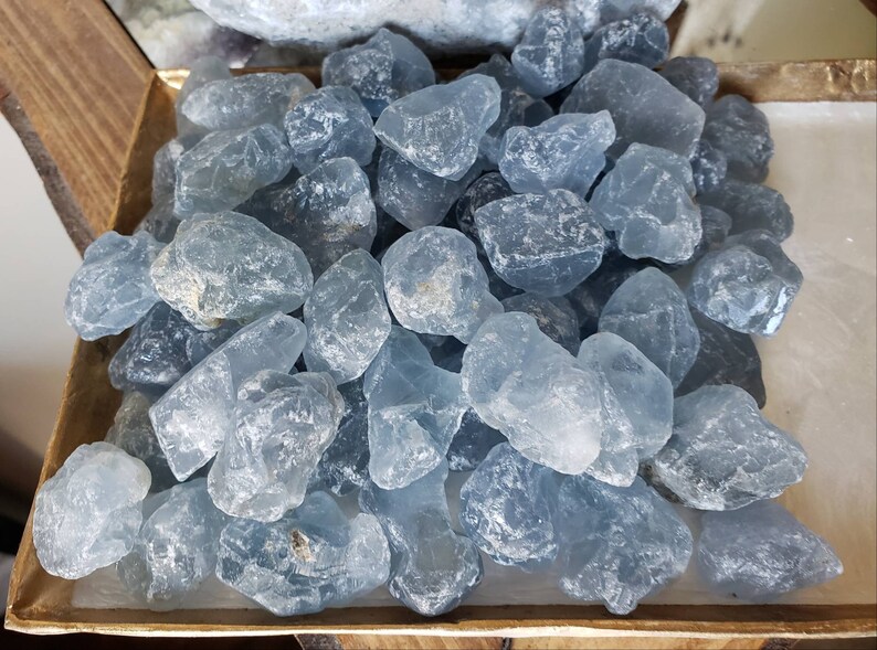 Peut inclure: Une collection de pierres de calcite bleue brutes et polies avec un aspect cristallin translucide. Les pierres varient en taille et en forme, pr&eacute;sentant des nuances de bleu p&acirc;le &agrave; moyen avec des fractures internes naturelles et des surfaces lisses.