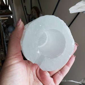 Op de afbeelding: Een wit selenietkristal met een hol midden, dat lijkt op een kom of een beker. Het kristal is glad en gepolijst, met een doorschijnende uitstraling.