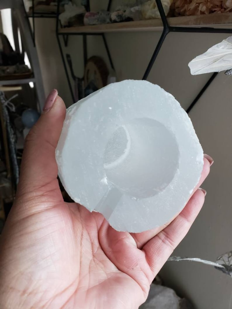 Op de afbeelding: Een wit selenietkristal met een hol midden, dat lijkt op een kom of een beker. Het kristal is glad en gepolijst, met een doorschijnende uitstraling.