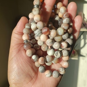 Op de afbeelding: Een set van vier armbanden gemaakt met agaat kralen. De kralen zijn een mix van bruin, wit en roze met draaiende patronen. De armbanden zijn geregen op elastisch koord en hebben zilveren kraal accenten.