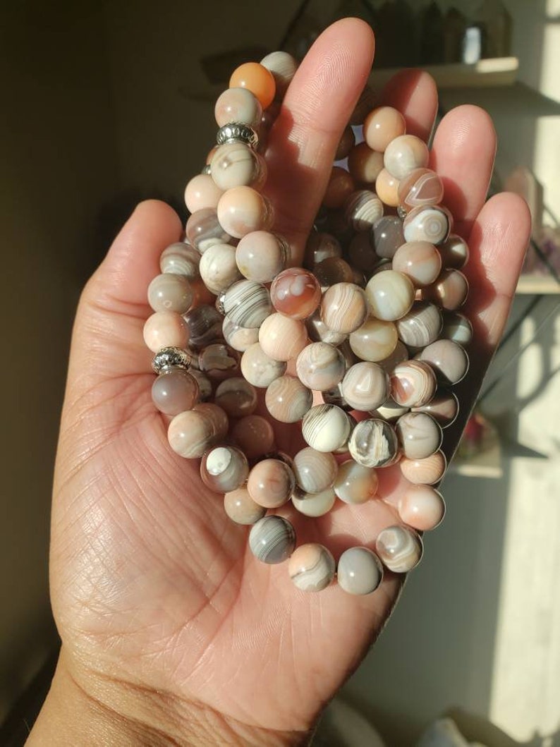 Op de afbeelding: Een set van vier armbanden gemaakt met agaat kralen. De kralen zijn een mix van bruin, wit en roze met draaiende patronen. De armbanden zijn geregen op elastisch koord en hebben zilveren kraal accenten.