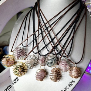 May include: A set of necklaces with caged crystal ball pendants. The pendants are available in two sizes, labeled "Large size" and "Medium size". The necklaces are made with brown and black cords.