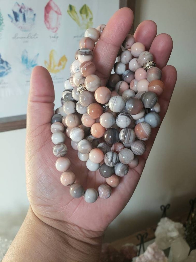 Op de afbeelding: Een stapel armbanden gemaakt van roze, witte en grijze agaat kralen. De kralen hebben een draaiende patroon en zijn geregen op elastiek.