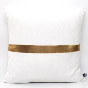 May include: White pillow with a gold satin ribbon across the center.