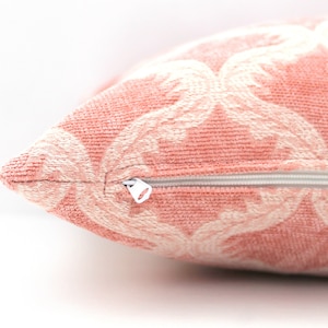 Pode incluir: Uma almofada rosa com um padr&atilde;o floral branco e um fecho de correr.