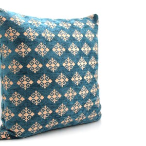 K&ouml;nnte beinhalten: Ein blauer Dekokissenbezug in Teal mit einem geometrischen Muster in hellem Pfirsich.
