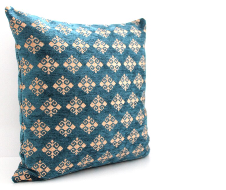 K&ouml;nnte beinhalten: Ein blauer Dekokissenbezug in Teal mit einem geometrischen Muster in hellem Pfirsich.