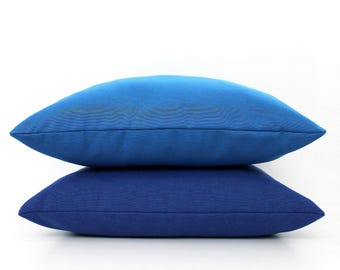 May include: Two square throw cushions stacked vertically. The top cushion is a bright, vibrant blue, while the bottom cushion is a deeper, darker navy blue. Both cushions feature a smooth, solid-coloured fabric finish with clean, stitched edges.