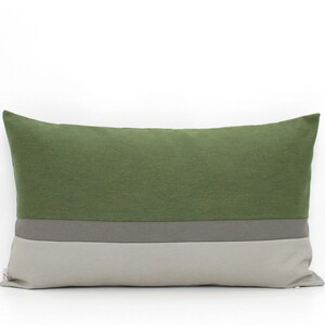 May include: A rectangular throw cushion featuring a colour-blocked design with a large olive green section on top, a narrow charcoal grey horizontal stripe in the middle, and a light grey section on the bottom, finished with a small side tag.