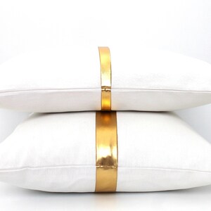 May include: Two white throw pillows with a gold stripe down the center.