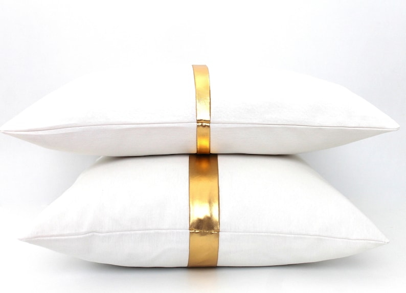 May include: Two white throw pillows with a gold stripe down the center.