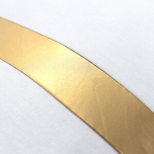 May include: A white pillow with a gold satin ribbon running diagonally across the front.