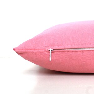 Puede incluir: Una almohada rosa con una cremallera blanca. La almohada est&aacute; hecha de una tela suave y texturizada.