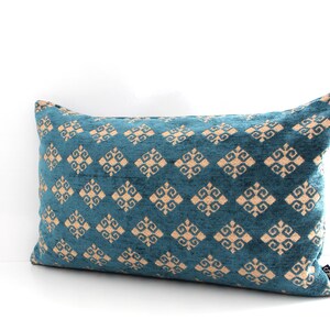 K&ouml;nnte beinhalten: Ein blaues Lendenkissen mit einem geometrischen Muster in hellbeige. Das Muster ist eine sich wiederholende Diamantform mit einem stilisierten Design in jedem Diamanten.