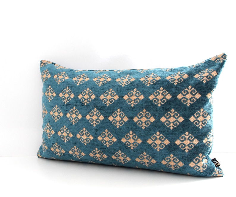 K&ouml;nnte beinhalten: Ein blaues Lendenkissen mit einem geometrischen Muster in hellbeige. Das Muster ist eine sich wiederholende Diamantform mit einem stilisierten Design in jedem Diamanten.
