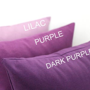 May include: Three rectangular cushions in shades of purple, from light lilac to dark purple. The text "LILAC", "PURPLE", and "DARK PURPLE" are printed on the cushions. The cushions are made of a solid-colored fabric.