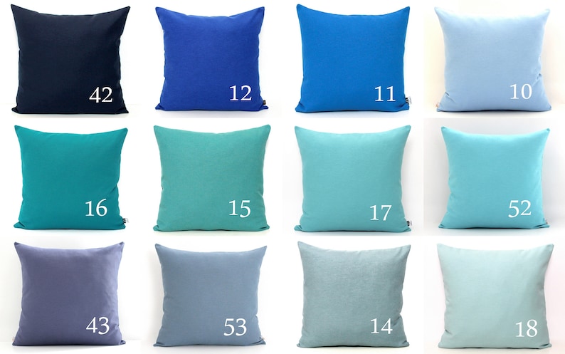 K&ouml;nnte beinhalten: Eine Sammlung von zw&ouml;lf quadratischen Zierkissen in verschiedenen Blau- und T&uuml;rkist&ouml;nen. Jedes Kissen hat eine einfarbige Farbe und eine wei&szlig;e Nummer in der Ecke. Die Farben reichen von Marineblau bis Hellblau und Aqua.