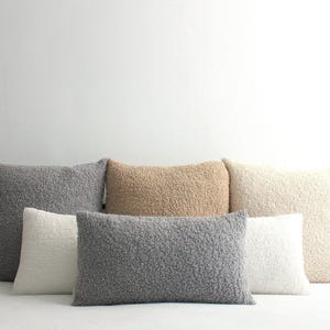 May include: A collection of six square and rectangular throw pillows featuring a textured, curly sherpa-style fabric. The pillows are arranged in two rows and come in various neutral shades including light gray, dark gray, beige, and off-white.