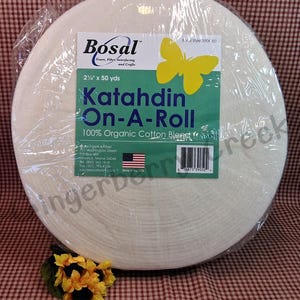 Puede incluir: Un rollo de entretela Katahdin On-A-Roll 100% algod&oacute;n org&aacute;nico de Bosal. El rollo mide 5,7 cm de ancho y 45,7 metros de largo. El embalaje incluye una etiqueta verde y blanca con una mariposa amarilla.