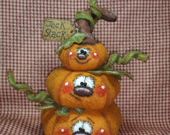 May include: A stacked pumpkin decoration with three orange pumpkins, each with a smiling face, rosy cheeks, and white eyes. Green vines and a brown stem top the pumpkins. A small tag reads "Jack Stack".