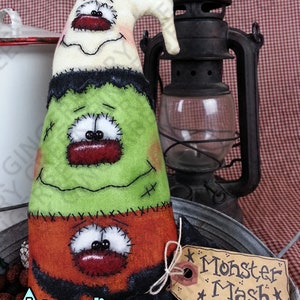May include: A handmade Halloween decoration shaped like a monster, with a white head, green middle, and orange bottom. Each section has stitched-on eyes and a red mouth. A tag reads "Monster Mash".