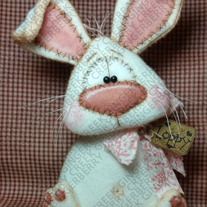 May include: A handmade white bunny with pink accents, including inner ears, nose, and paws. The bunny has black bead eyes, whiskers, and a pink floral bow. A small tag reads "Loppy". The bunny is a decorative item.