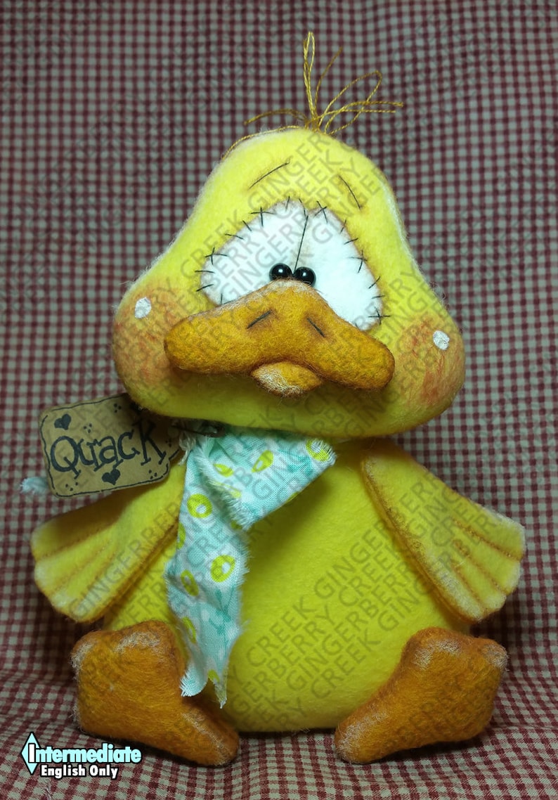 May include: A handmade yellow duck plush toy with a large orange beak and feet. It has a white face with black eyes and a blue and white patterned scarf. A tag that says "Quack" hangs from its neck.