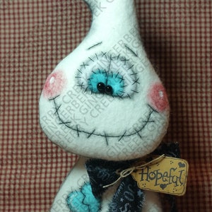 May include: A handmade white ghost doll with stitched details, rosy cheeks, and a stitched smile. It has blue eyes and a black bow with a tag that says "Hopeful". The doll is a whimsical Halloween decoration.