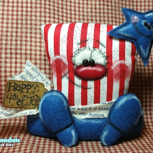 May include: A patriotic plush figure with a red, white, and blue color scheme. The figure has a popcorn box body with a smiling face, blue feet, and a blue star. A tag reads "Happy 4th of July".