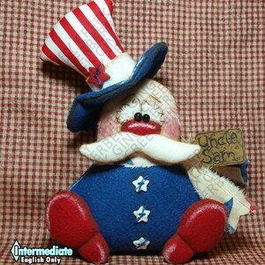 Könnte beinhalten: Eine handgefertigte Uncle Sam-Puppe in Rot, Weiß und Blau. Die Puppe hat einen gestreiften Zylinder, einen blauen Mantel mit sternförmigen Knöpfen und rote Schuhe. Ein kleines Schild trägt die Aufschrift "Uncle Sam".