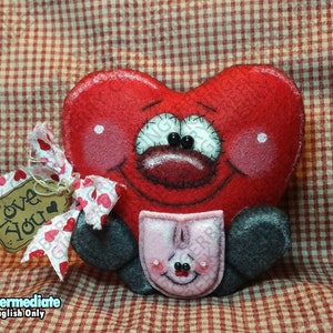 Könnte beinhalten: Ein rotes herzförmiges Plüschtier mit einem lächelnden Gesicht, rosigen Wangen und schwarzen Augen. Es hält eine rosa Tasche mit einem lächelnden Gesicht. Ein Anhänger mit "Love You" ist mit einem Band am Herzen befestigt. Der Hintergrund ist ein rot-weiß kariertes Muster.