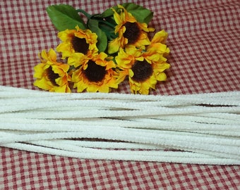 May include: A collection of white pipe cleaners arranged on a red and white checkered surface. A bouquet of yellow sunflowers with brown centers and green leaves is in the background. These craft supplies are ideal for various DIY projects.