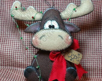 May include: A handmade felt moose with a red bow and a string of lights. The moose has large antlers and a tag that says "Oops". The moose is brown, tan, and red, and is sitting on a red and white checkered background.